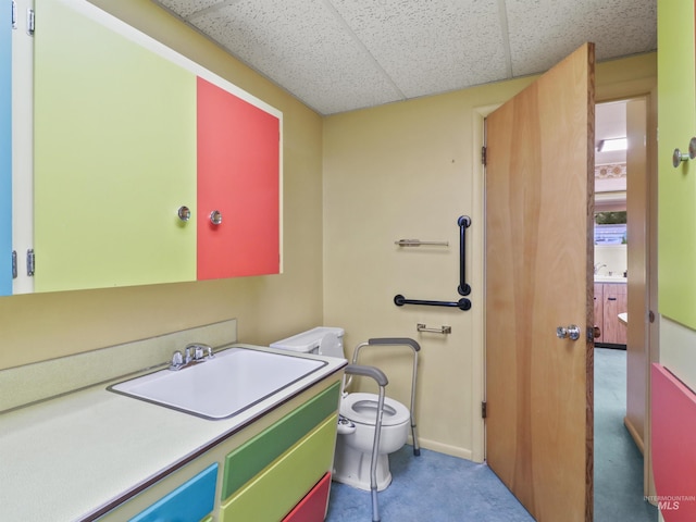 bathroom featuring vanity, toilet, and a drop ceiling