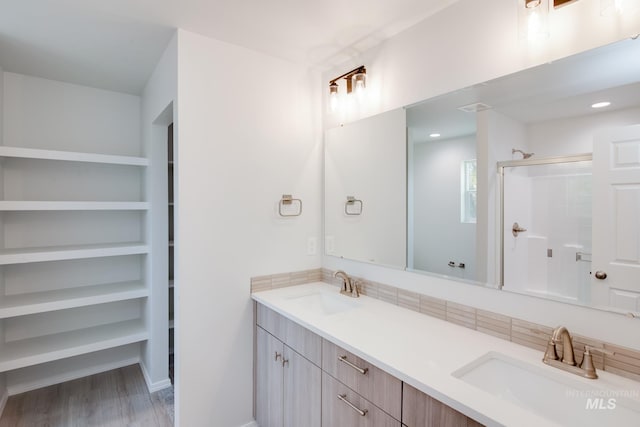 full bath with a stall shower, wood finished floors, a sink, and double vanity