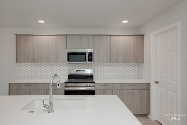 kitchen with stainless steel appliances, modern cabinets, a sink, and light countertops