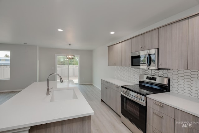 kitchen with stainless steel appliances, a sink, light countertops, backsplash, and modern cabinets