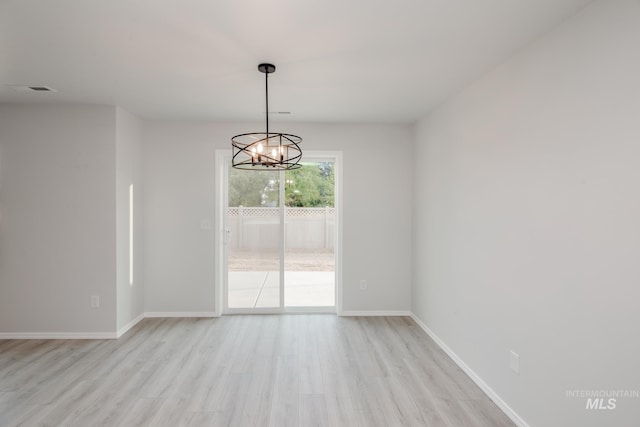 spare room featuring light wood-style floors, a notable chandelier, and baseboards