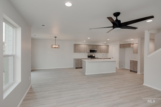 kitchen featuring a kitchen island with sink, appliances with stainless steel finishes, light wood finished floors, modern cabinets, and tasteful backsplash