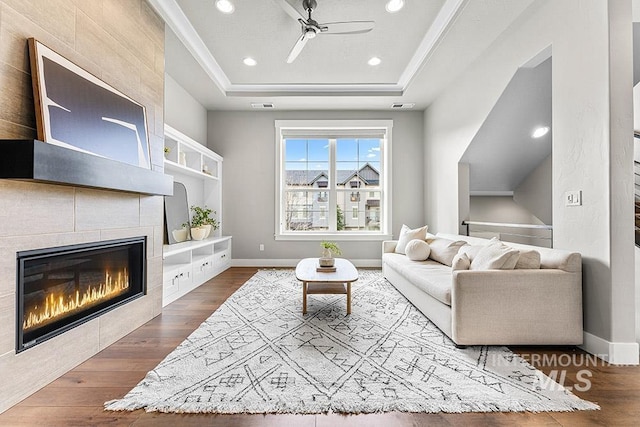 living room featuring a tiled fireplace, a raised ceiling, and dark wood-type flooring