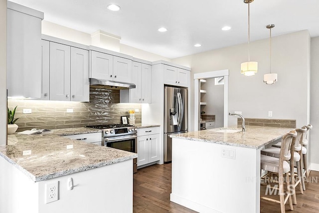 kitchen featuring stainless steel appliances, hanging light fixtures, a sink, a peninsula, and under cabinet range hood