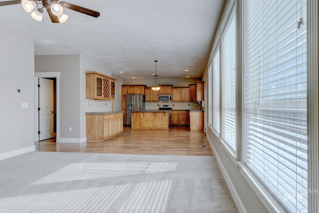 kitchen with appliances with stainless steel finishes, a textured ceiling, decorative light fixtures, a kitchen island, and light colored carpet