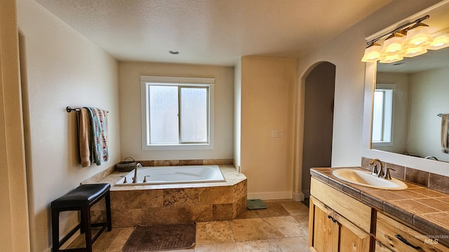 bathroom with a textured ceiling, a relaxing tiled tub, plenty of natural light, and vanity