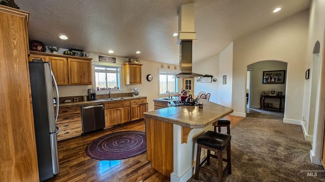 kitchen featuring tile countertops, a center island, a kitchen bar, appliances with stainless steel finishes, and island range hood