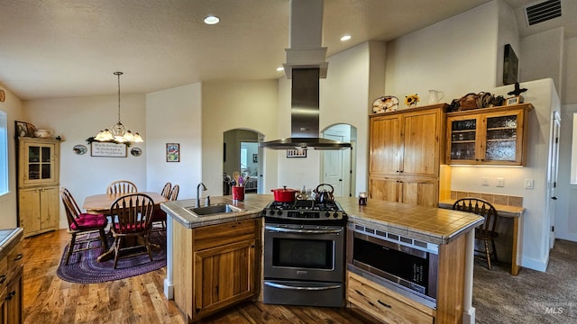 kitchen with sink, a kitchen island with sink, stainless steel appliances, tile counters, and island range hood