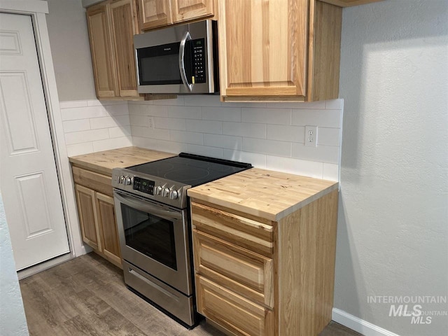 kitchen with butcher block countertops, appliances with stainless steel finishes, dark wood-style floors, and backsplash