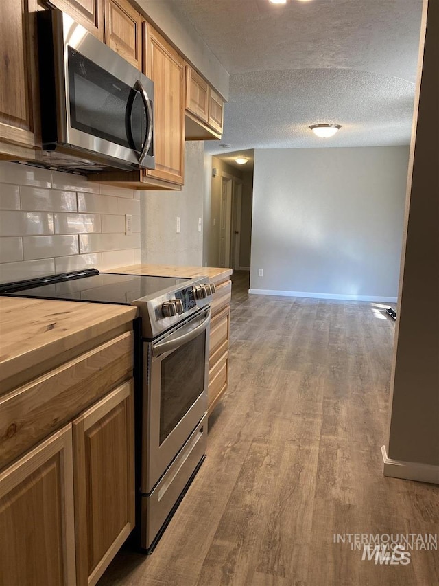 kitchen with butcher block counters, a textured ceiling, wood finished floors, stainless steel appliances, and decorative backsplash