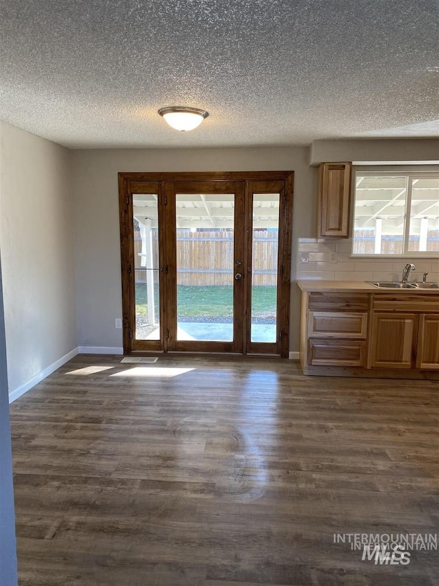 unfurnished dining area with dark wood-style flooring, baseboards, a sink, and a textured ceiling