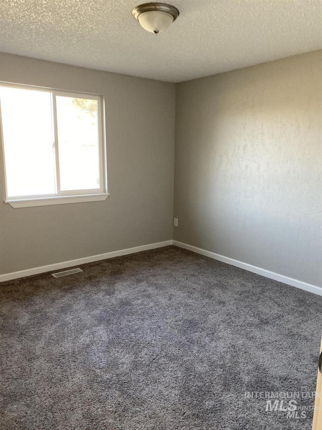 carpeted empty room featuring a textured ceiling, baseboards, and visible vents