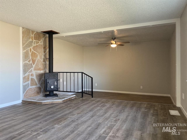 spare room with a textured ceiling, wood finished floors, a wood stove, and a ceiling fan