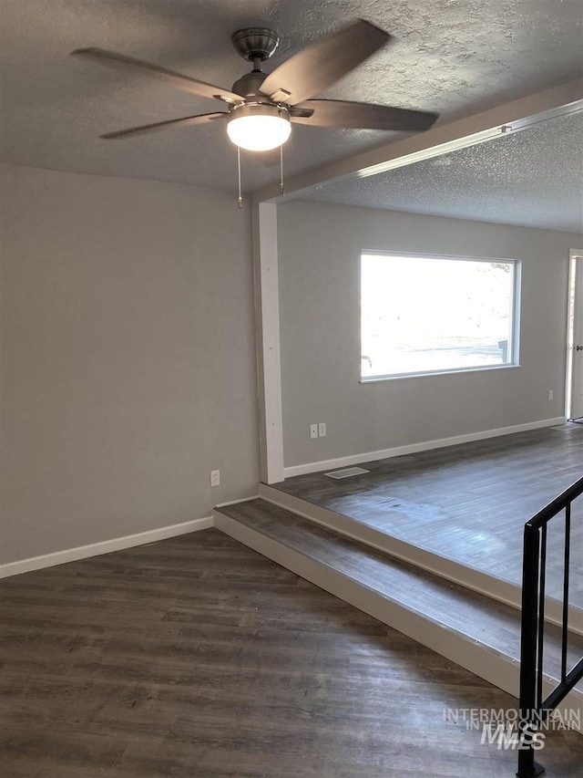 empty room with dark wood-style flooring, a textured ceiling, baseboards, and ceiling fan