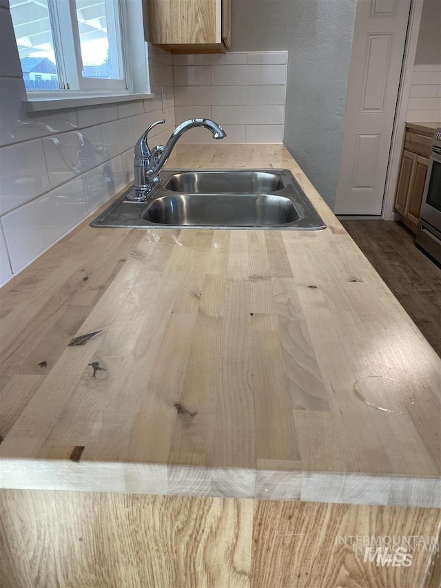 kitchen featuring a sink, butcher block countertops, decorative backsplash, and stainless steel stove