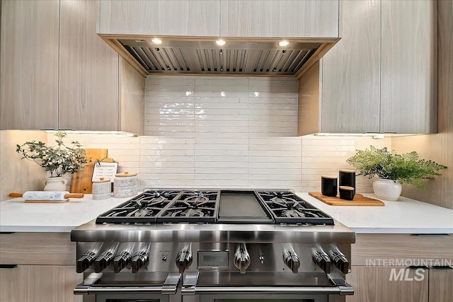 kitchen featuring stove, light brown cabinets, light stone counters, and wall chimney range hood