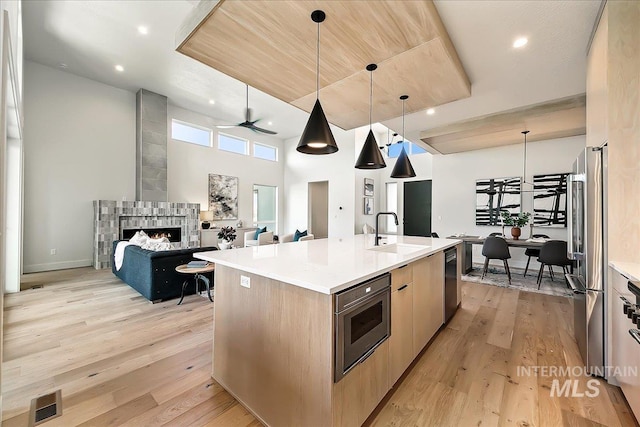 kitchen with a kitchen island with sink, a tile fireplace, sink, ceiling fan, and decorative light fixtures