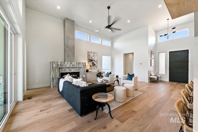 living room featuring ceiling fan, a towering ceiling, a tile fireplace, and light hardwood / wood-style flooring