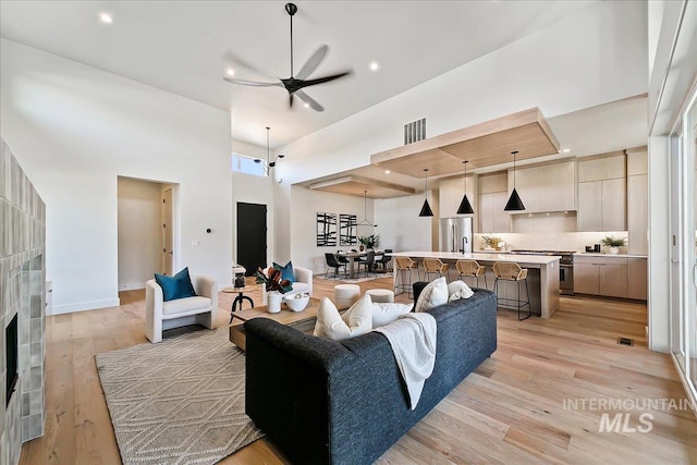 living room featuring ceiling fan, a fireplace, light hardwood / wood-style floors, and a high ceiling