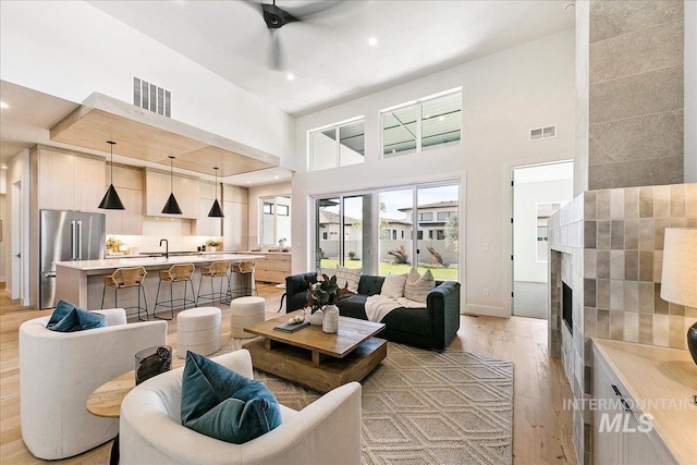 living room with ceiling fan, sink, a high ceiling, and light hardwood / wood-style flooring