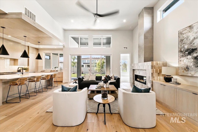 living room featuring ceiling fan, a fireplace, a high ceiling, and light wood-type flooring