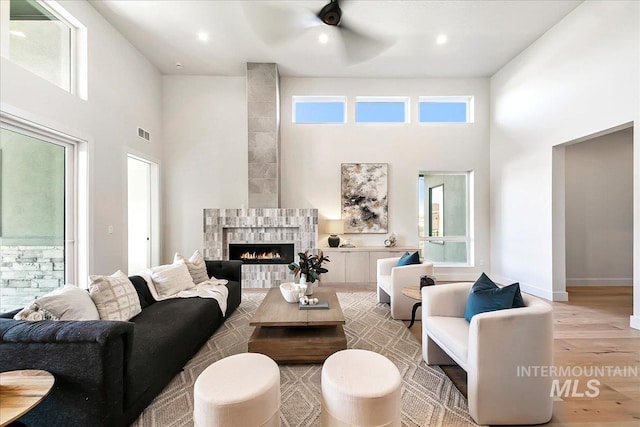 living room with a high ceiling, light hardwood / wood-style floors, ceiling fan, and a tiled fireplace