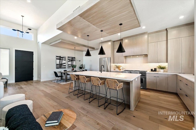 kitchen with hanging light fixtures, light hardwood / wood-style floors, a chandelier, a center island with sink, and high end appliances