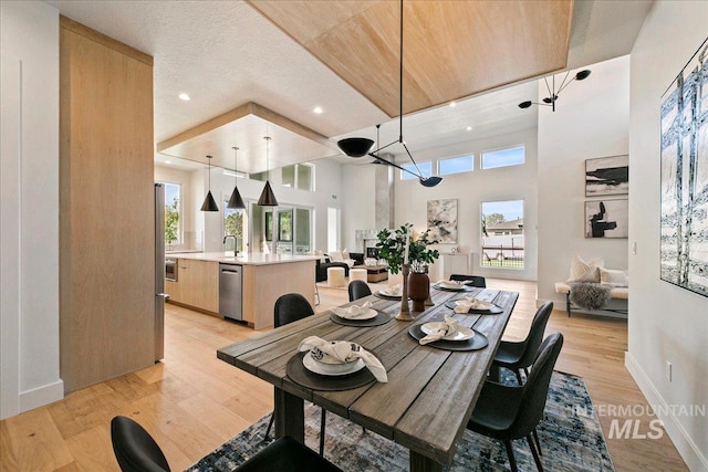 dining room with sink, a towering ceiling, a textured ceiling, and light wood-type flooring