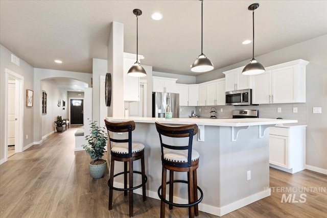 kitchen featuring light countertops, arched walkways, appliances with stainless steel finishes, and a kitchen bar