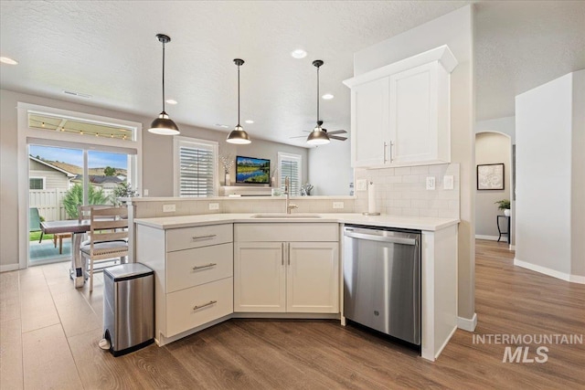 kitchen with backsplash, stainless steel dishwasher, a sink, light countertops, and dark wood-type flooring