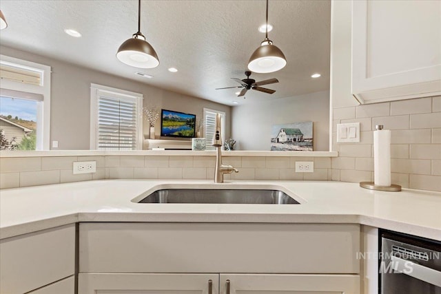 kitchen featuring decorative light fixtures, stainless steel dishwasher, a sink, recessed lighting, and white cabinetry