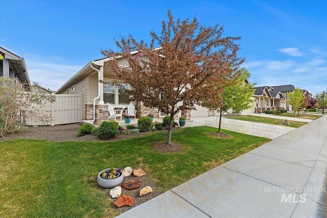 view of front facade featuring driveway, a front yard, a residential view, fence, and stone siding