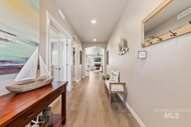hallway featuring visible vents, arched walkways, baseboards, and light wood-type flooring