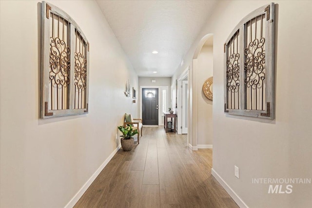 corridor with recessed lighting, baseboards, arched walkways, and hardwood / wood-style flooring