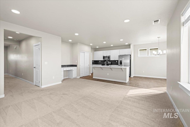 unfurnished living room with baseboards, visible vents, a notable chandelier, and recessed lighting