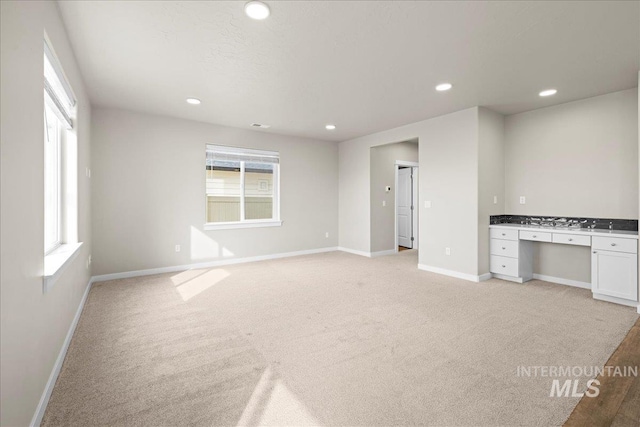 interior space featuring recessed lighting, baseboards, built in desk, and light colored carpet