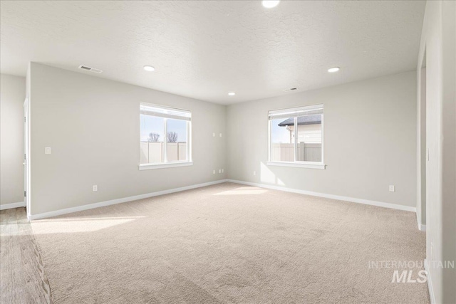 spare room featuring a wealth of natural light, visible vents, light carpet, and a textured ceiling