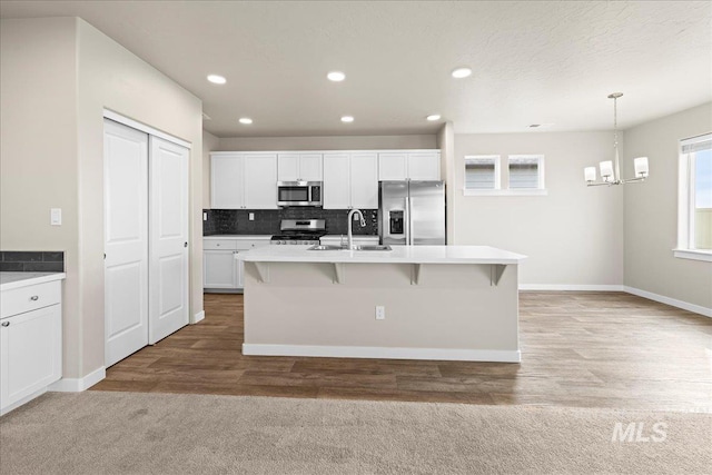 kitchen with stainless steel appliances, a sink, white cabinets, backsplash, and an island with sink