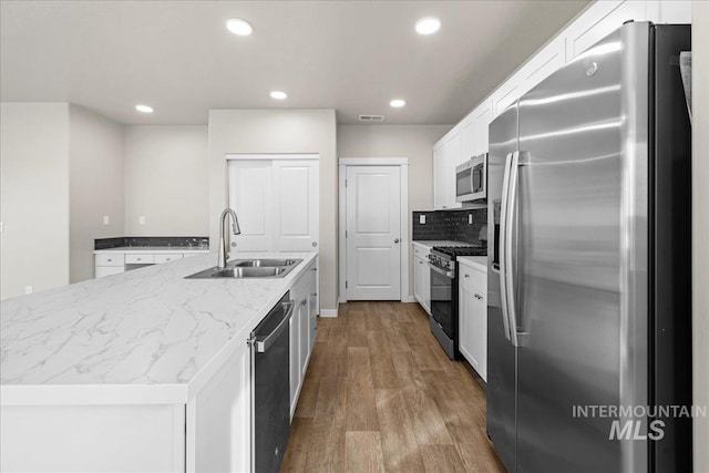 kitchen featuring appliances with stainless steel finishes, white cabinetry, a sink, an island with sink, and wood finished floors