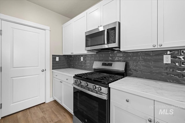 kitchen with light wood finished floors, stainless steel appliances, tasteful backsplash, and light stone countertops