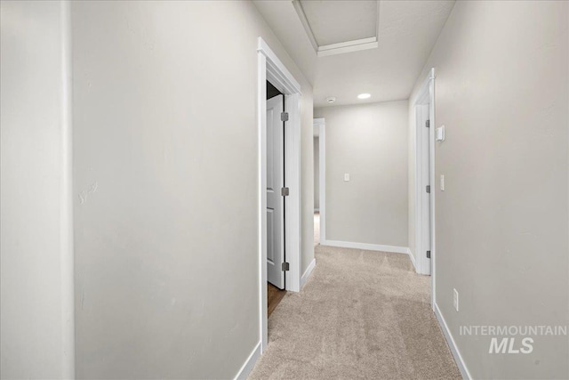 hallway with carpet, baseboards, and attic access