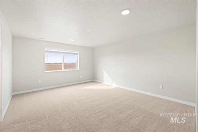 spare room with light carpet, a textured ceiling, recessed lighting, and baseboards