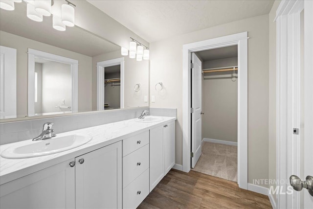 full bathroom featuring double vanity, a spacious closet, a sink, and wood finished floors