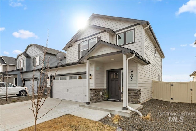 view of front of house with an attached garage, fence, driveway, stone siding, and a gate