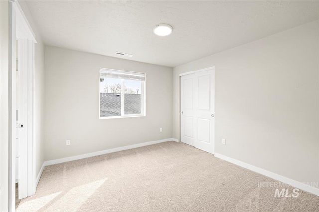 unfurnished bedroom with a textured ceiling, visible vents, baseboards, a closet, and carpet