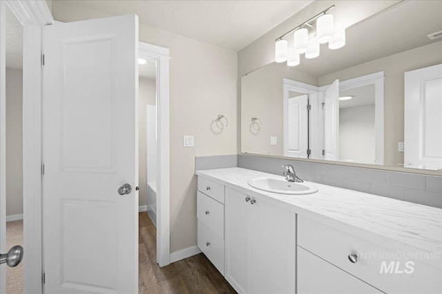 bathroom with baseboards, visible vents, a bathing tub, wood finished floors, and vanity