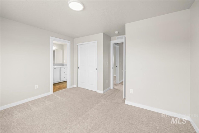 unfurnished bedroom featuring carpet, a closet, baseboards, and ensuite bathroom