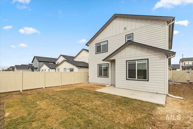 back of house with board and batten siding, a fenced backyard, a yard, and a patio