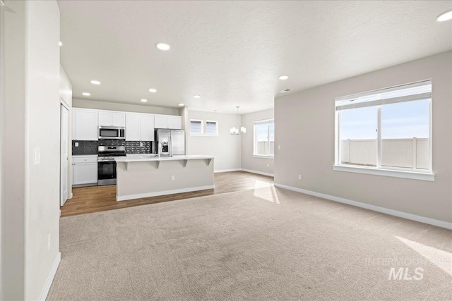 kitchen featuring a breakfast bar area, tasteful backsplash, light colored carpet, appliances with stainless steel finishes, and open floor plan