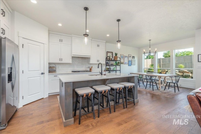 11328 W Campanula Dr, Star, ID 83669 - kitchen with stainless steel fridge, a sink, wood finished floors, white cabinets, and a chandelier
